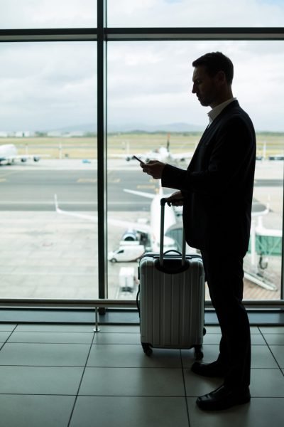 Businessman with luggage using mobile phone at airport